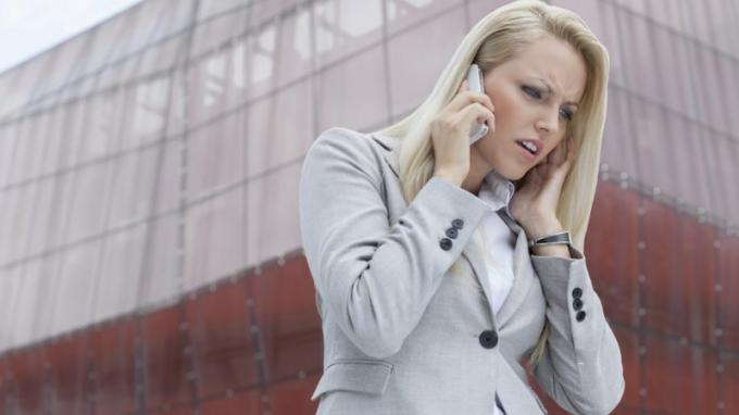 Nainen, jolla on ADHD, kuuntelee joku matkapuhelimesta ja suuttuu korkean rakennuksen edessä